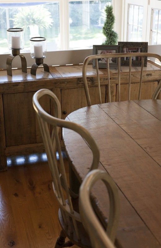 Wooden dining table with chairs in front of a weathered wood cabinet near a window with sunlight.