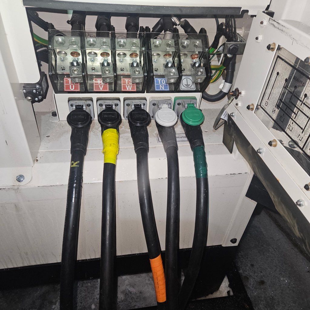 Five electrical cables plugged into a terminal block, labeled with colored tape for phase identification.