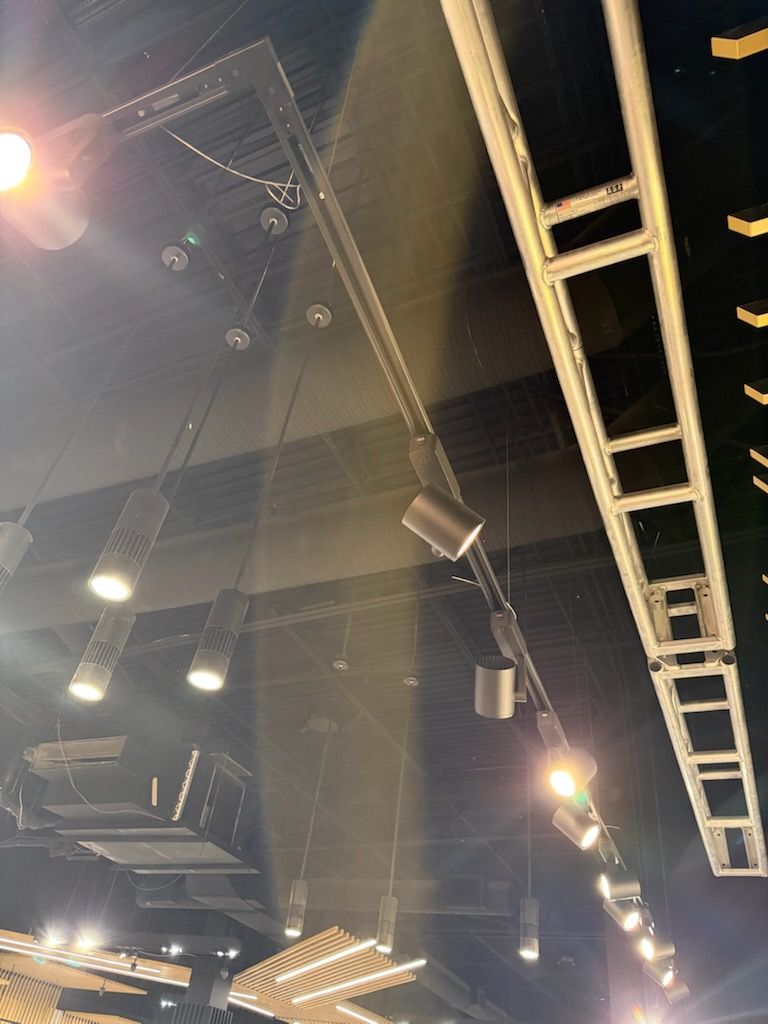 Low-angle view of industrial ceiling lighting, featuring multiple cylindrical spotlights attached to a dark metal frame.