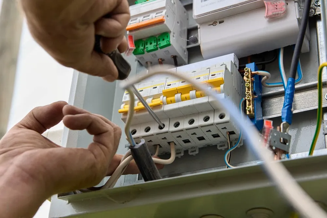 A technician uses a screwdriver to secure a white wire into a circuit breaker inside an electrical panel.