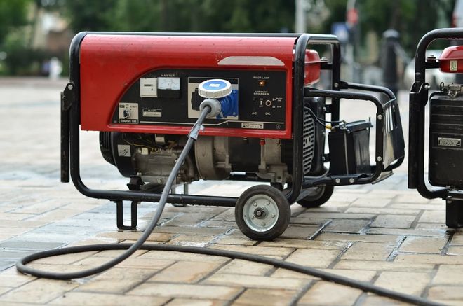 A portable red generator sits on a paved surface, plugged into a heavy-duty cable.