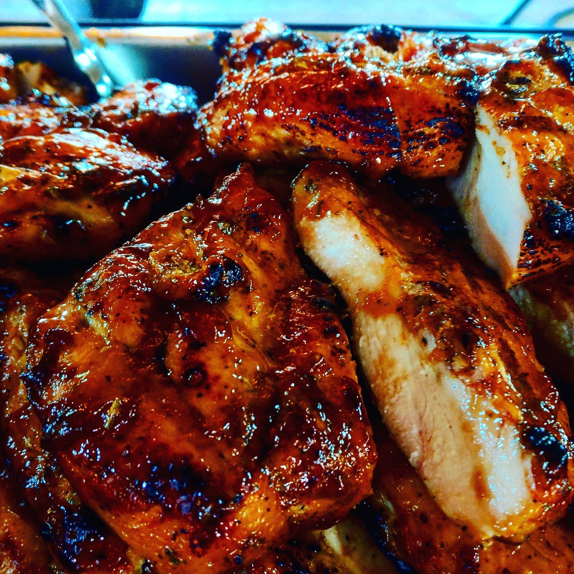 Close-up of a tray of juicy, grilled chicken breasts, glistening with a golden-brown char and seasoned with herbs