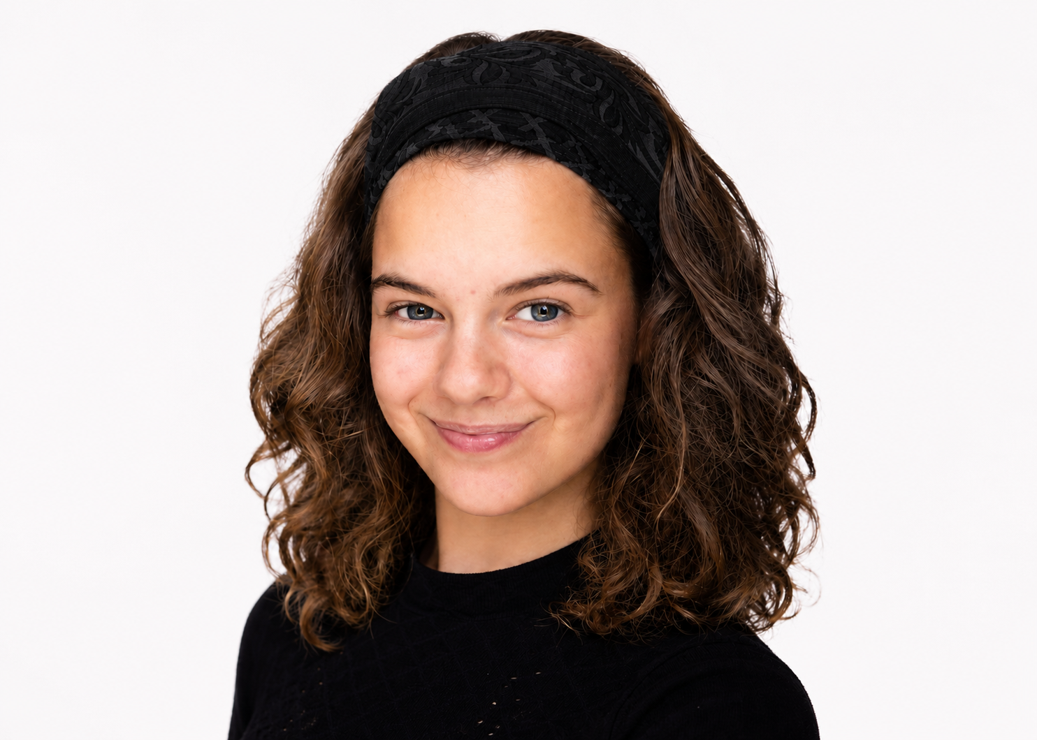 Portret van een lachend persoon met krullend donker haar, gekleed in een zwarte top, tegen een witte achtergrond.