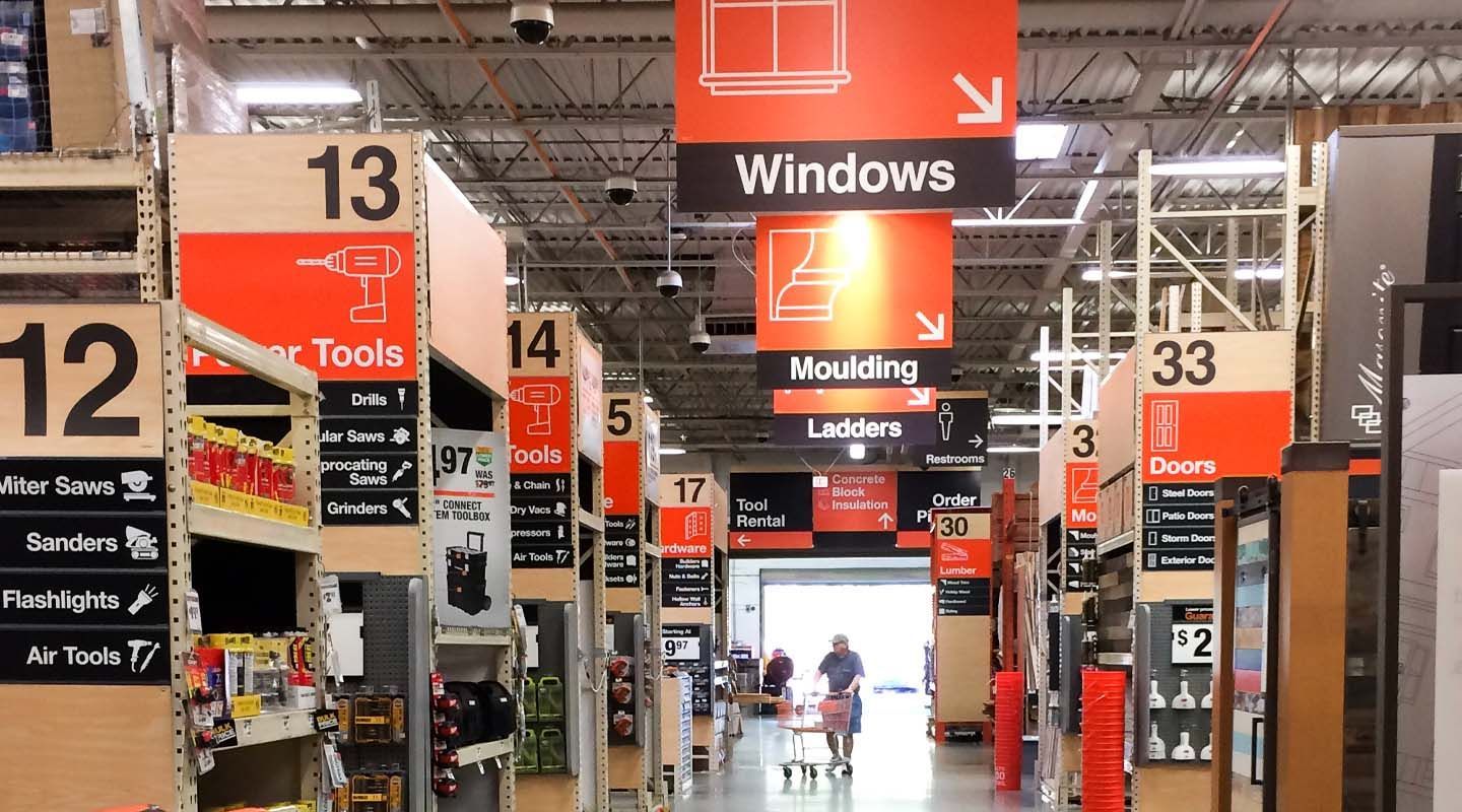 Store aisle with tall orange overhead signs and numbered sections in a warehouse-style retail store