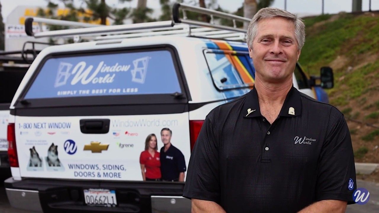 Man smiling beside a white utility truck with business graphics and a roadside backdrop