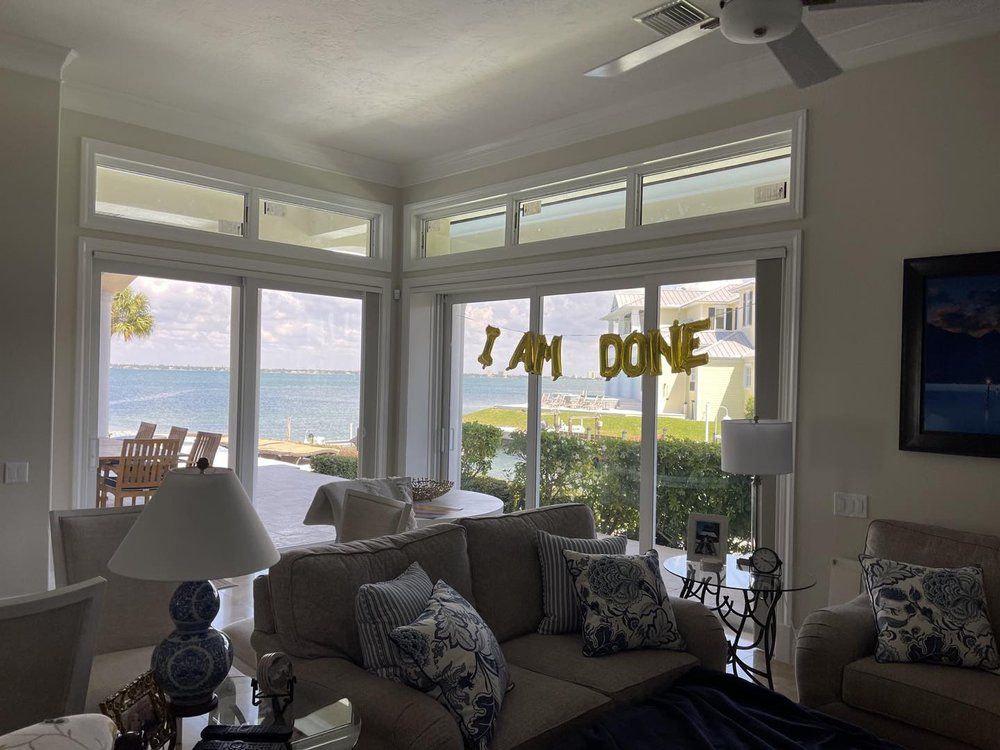 Bright coastal living room with large windows, ocean view, and “I AM DONE” balloons on the glass