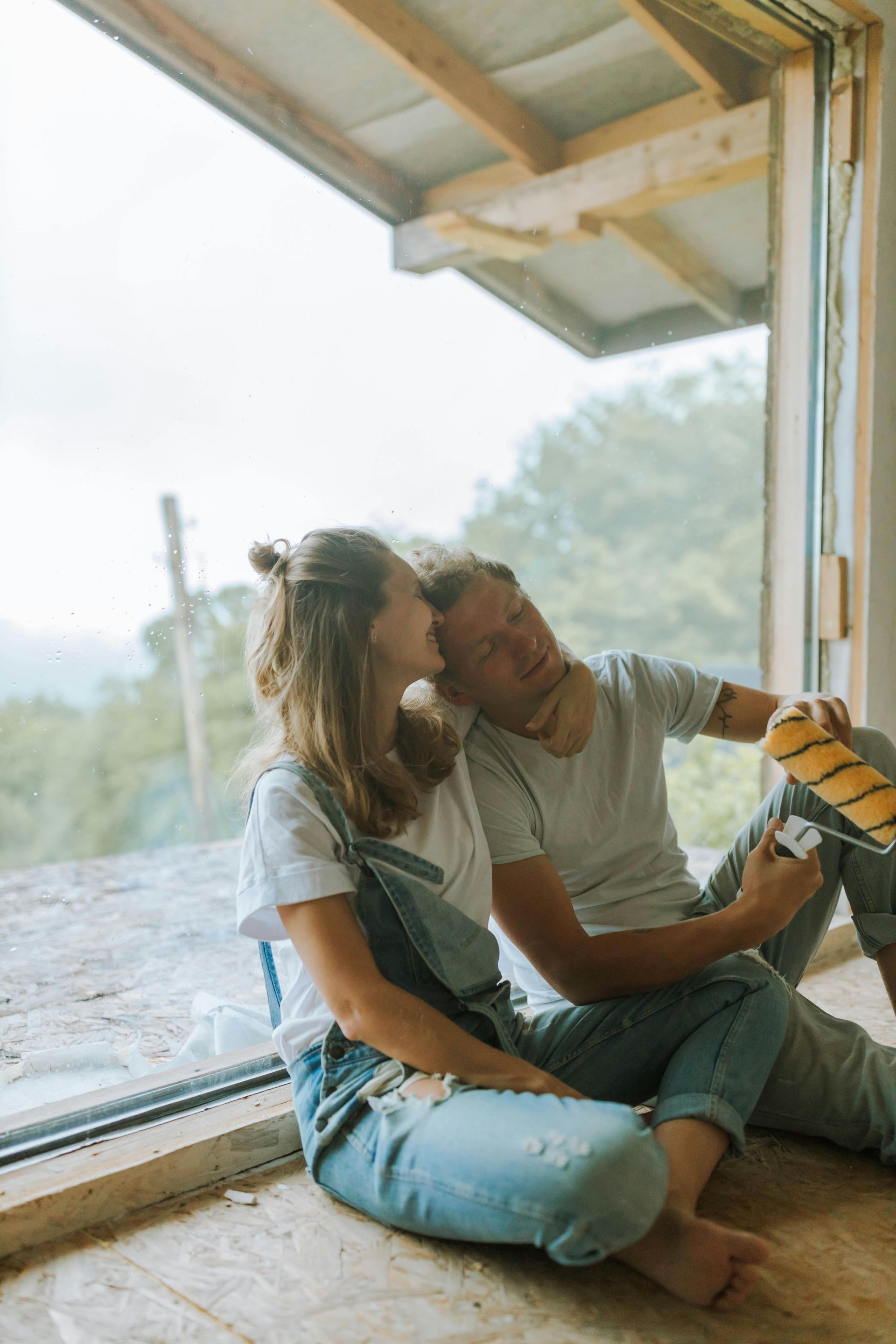 Two people sitting by an open window, leaning close together in a bright room
