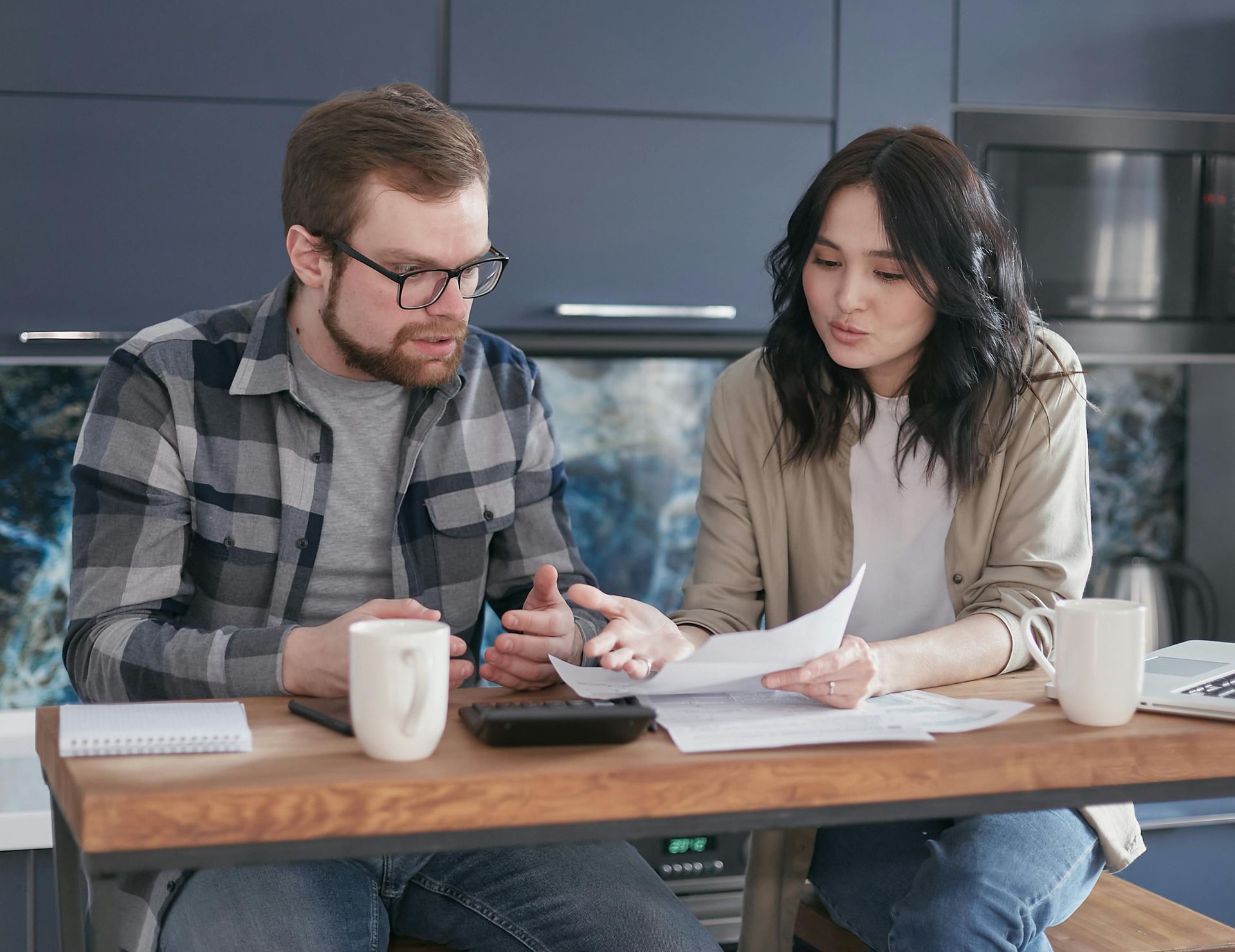 Couple reviewing paperwork together in kitchen, using calculator.