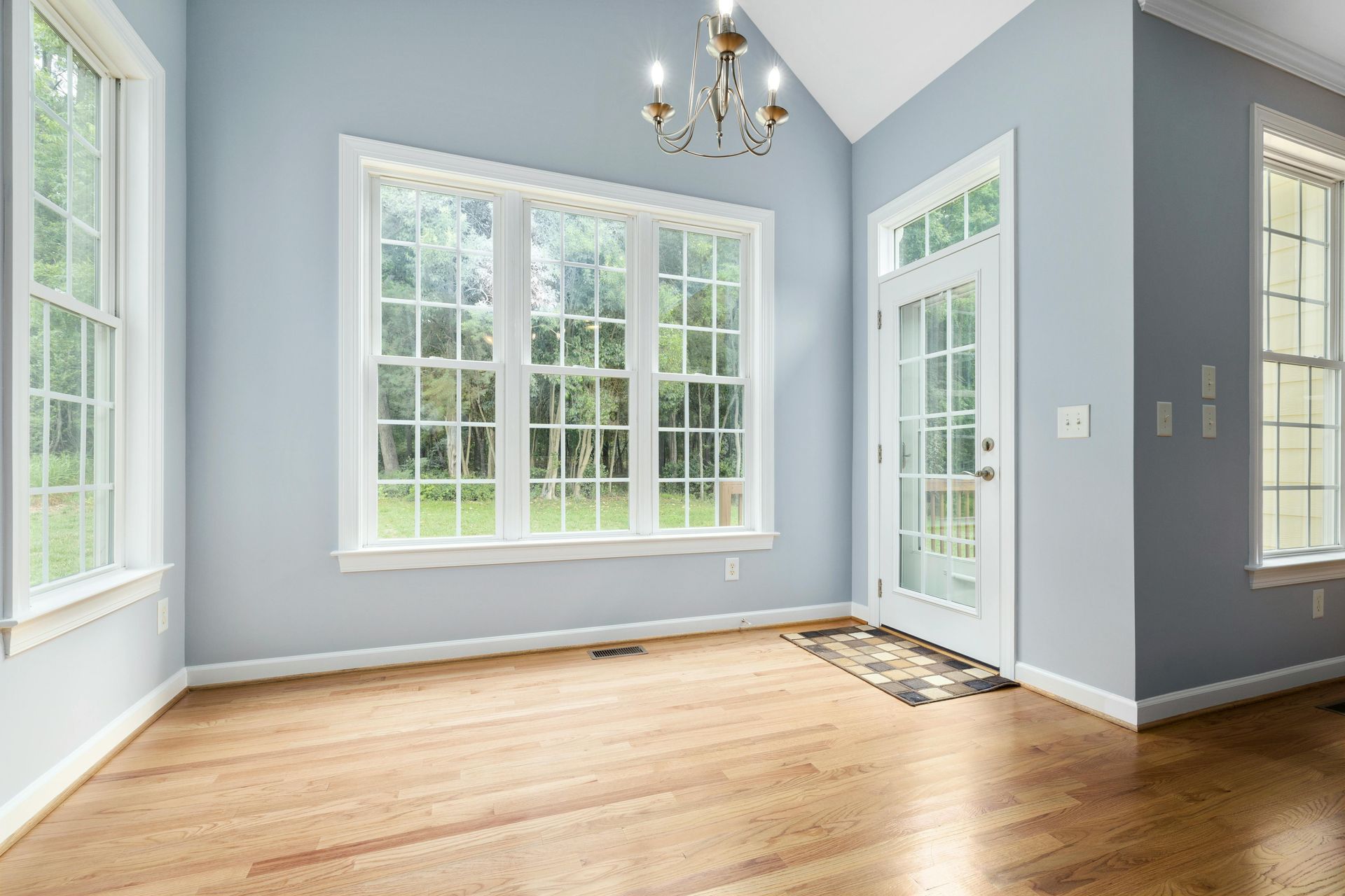 Bright empty dining room with large windows, light blue walls, and hardwood floors