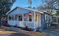 Small gray house with white trim and porch, an American flag hanging by the front door.