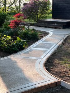 A concrete walkway in a garden next to a house.
