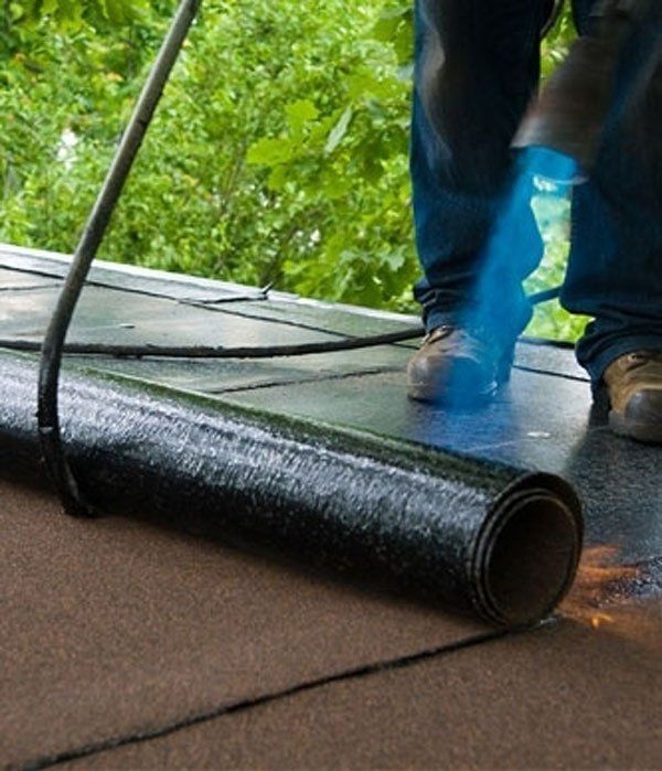 operaio mentre prepara parte del rotolo del feltro del tetto del bitume