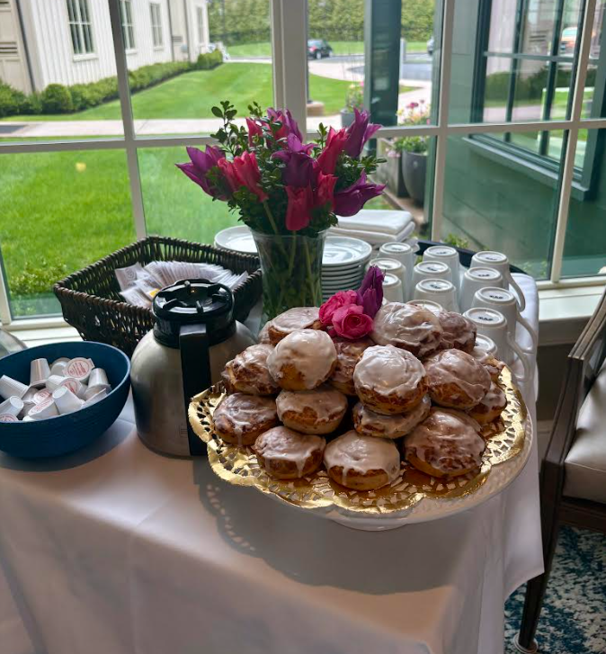 Pastries, flowers, and hot cinnamon buns on a table by large windows in a bright room