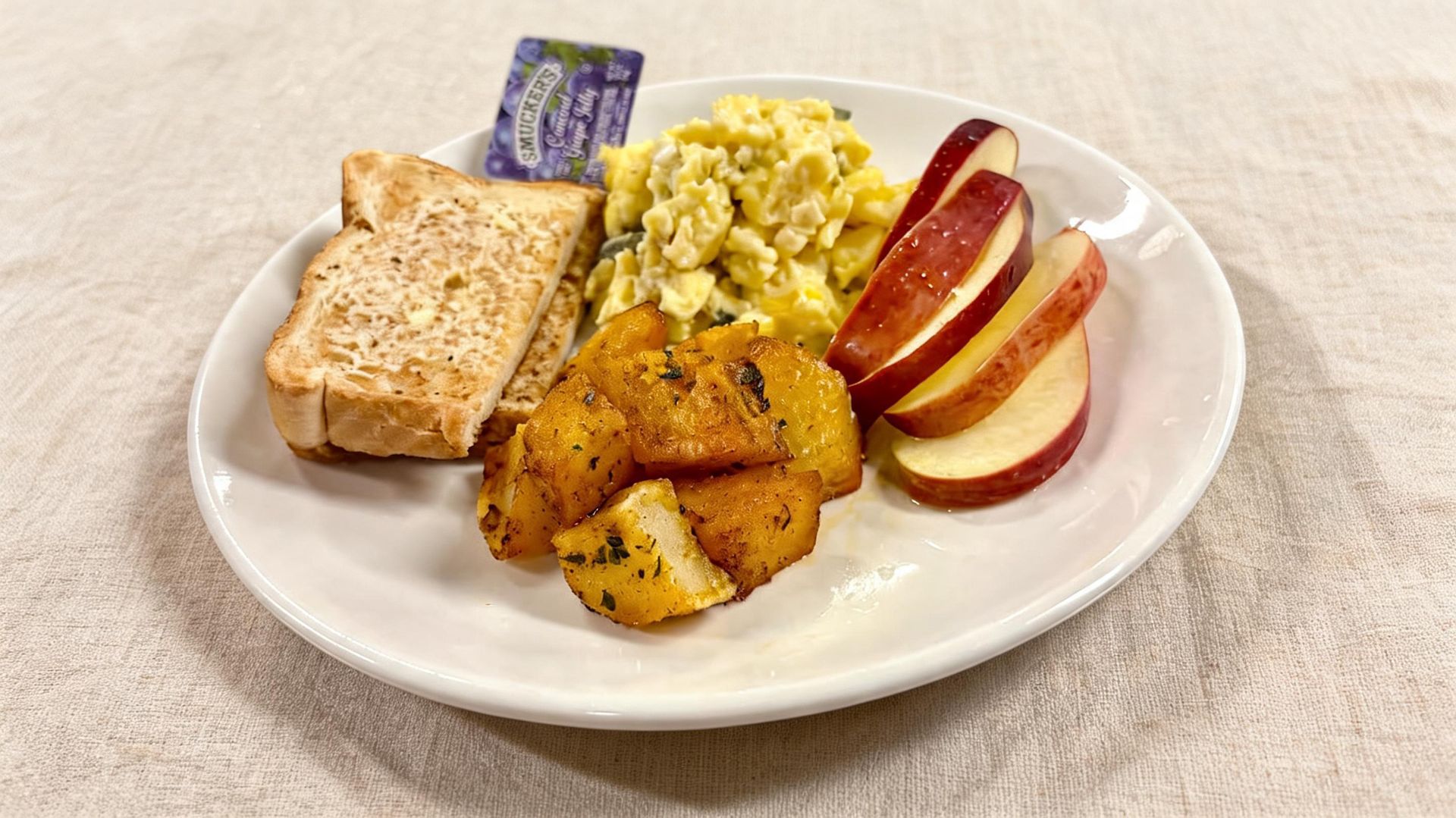 Plate with toast, scrambled eggs, roasted potatoes, and apple slices on a white dish
