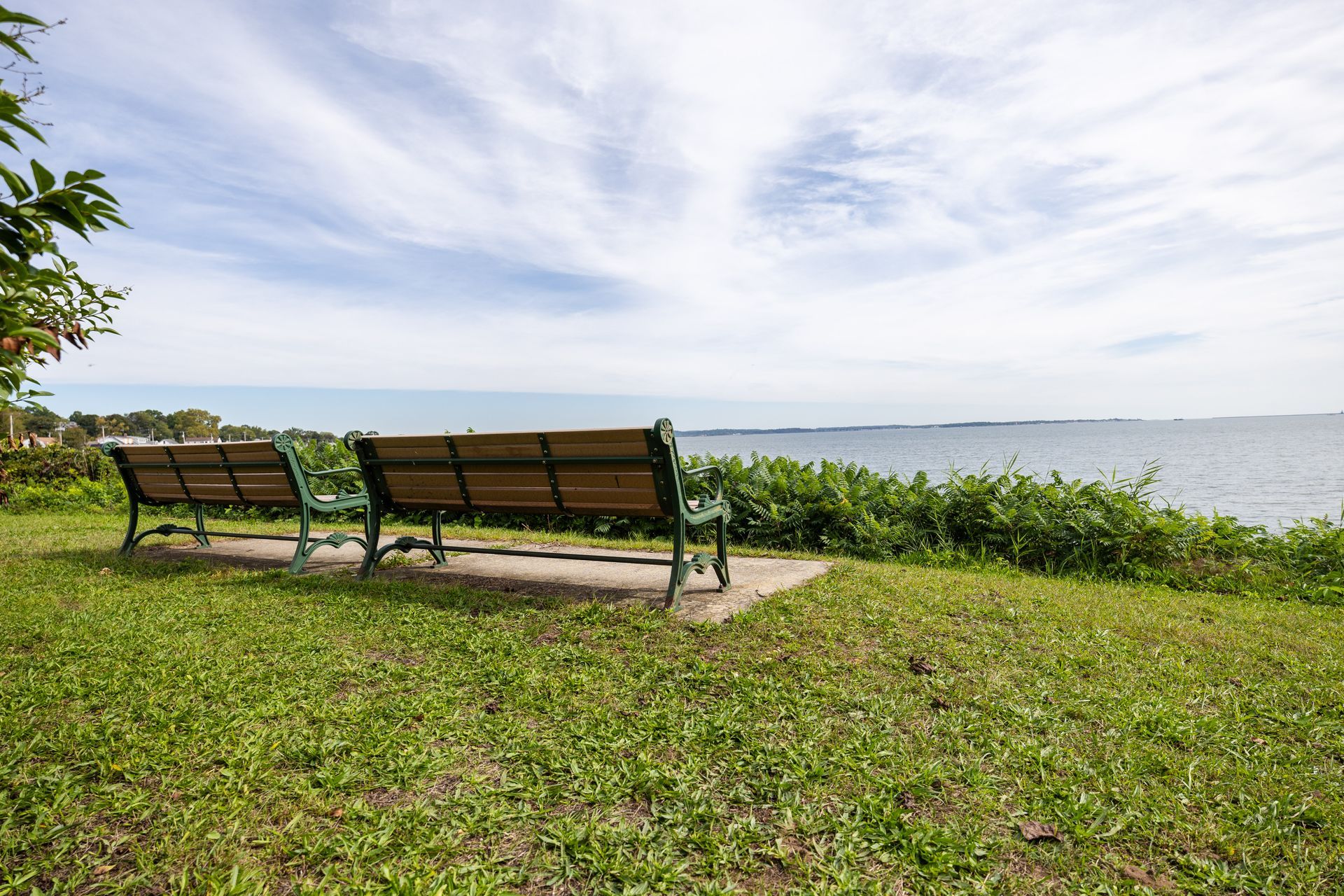 Two park benches on grassy hill overlooking a body of water under a cloudy sky.