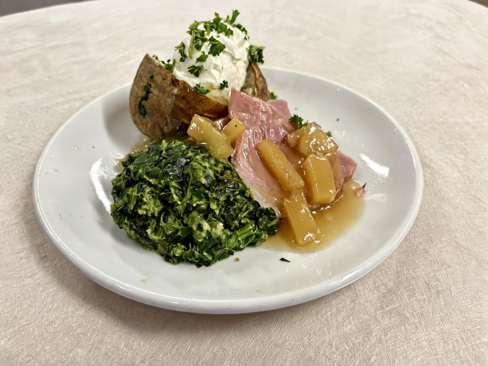 Plated gourmet dish with greens, roasted vegetables, and a stuffed potato topped with cream and herbs