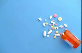 Orange pill bottle lying on its side, spilling assorted pills on a blue surface.