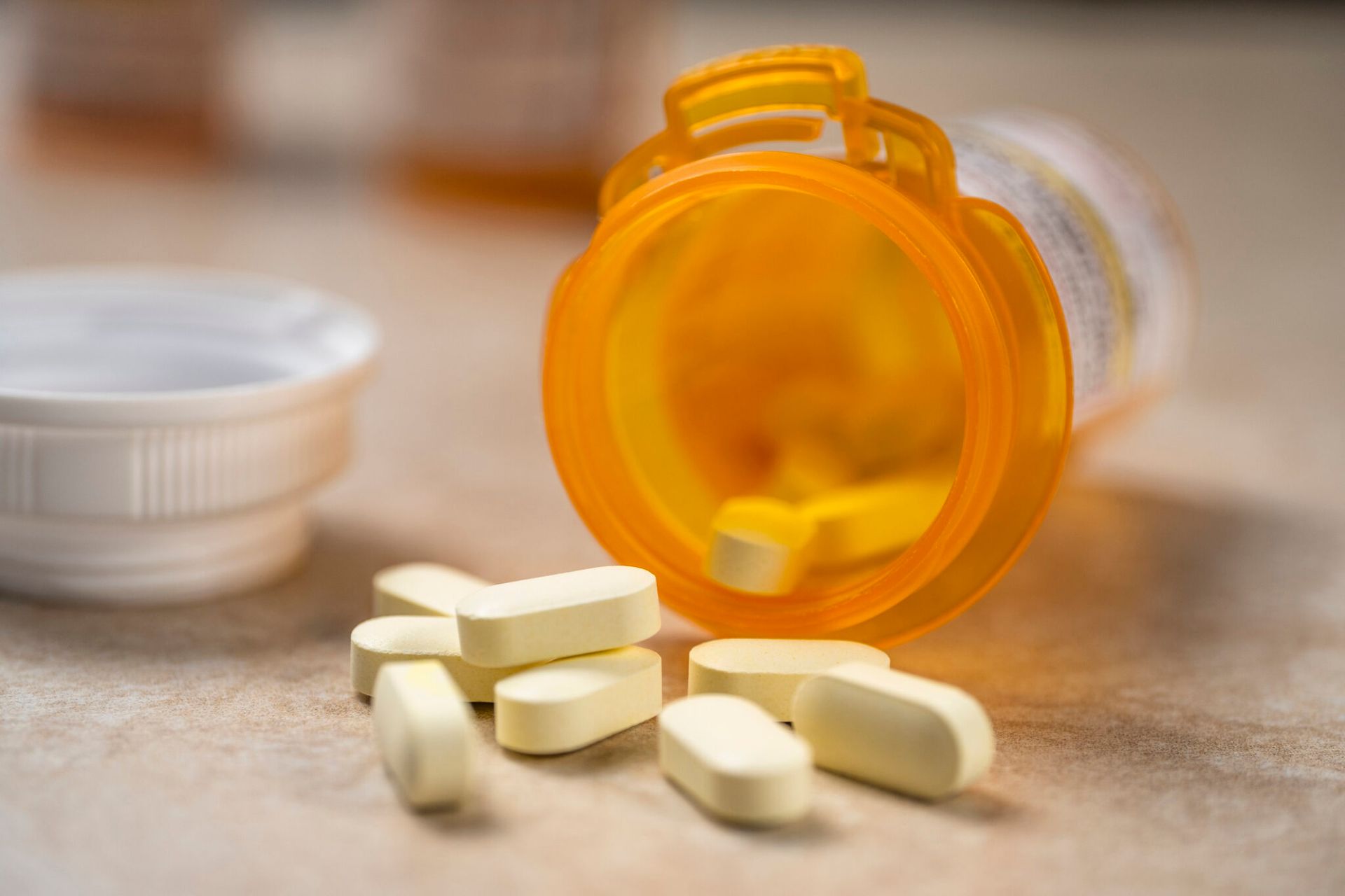 An orange prescription pill bottle tipped on its side with several yellow oblong tablets scattered on a table.