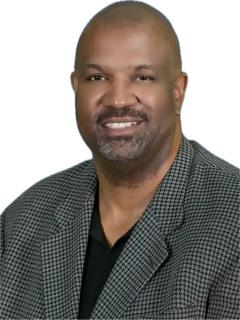 Man with a shaved head and a gray and black patterned blazer smiling at the camera.