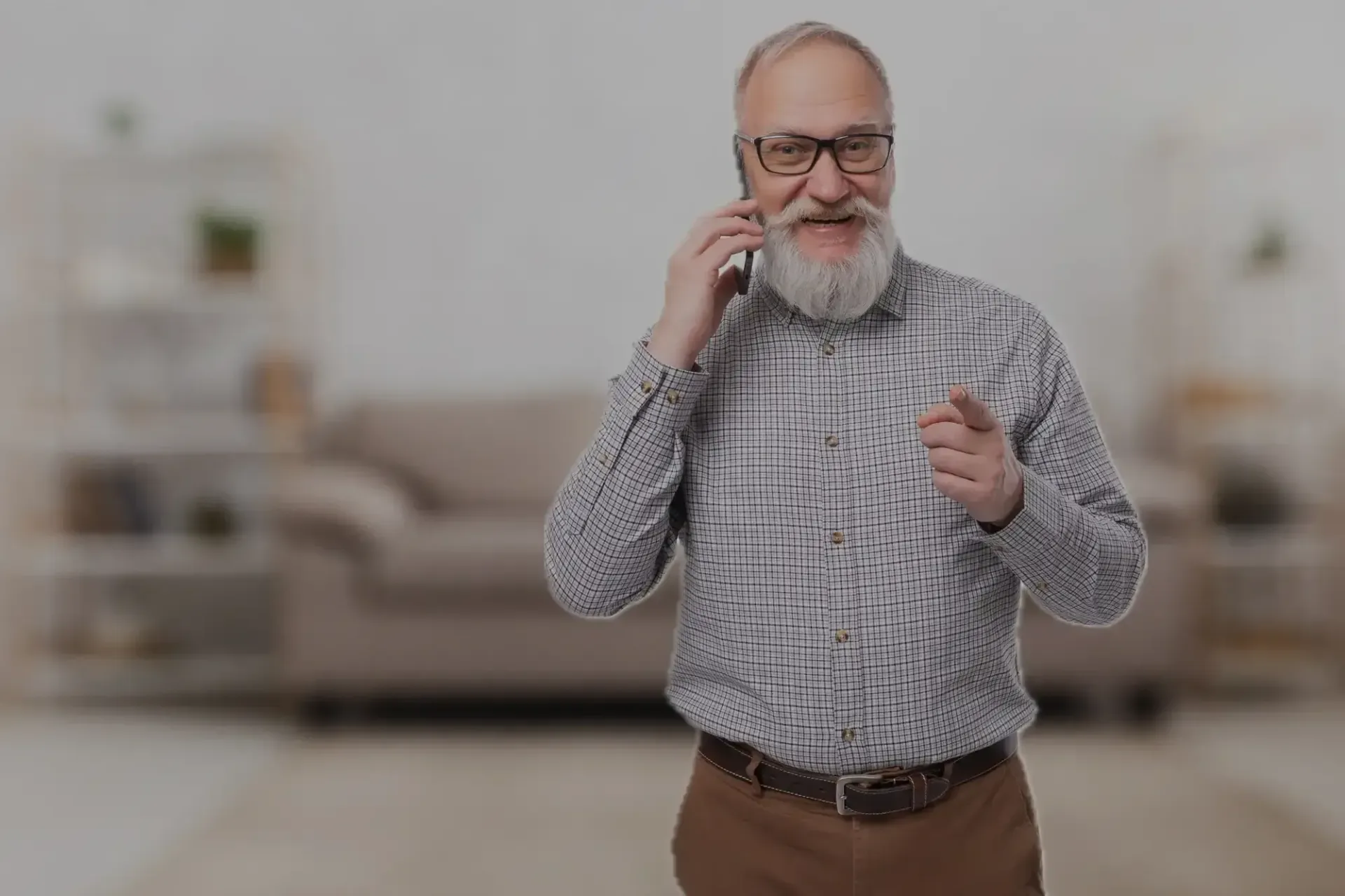 Man standing in a living room, talking on a phone and pointing, with a couch in the background
