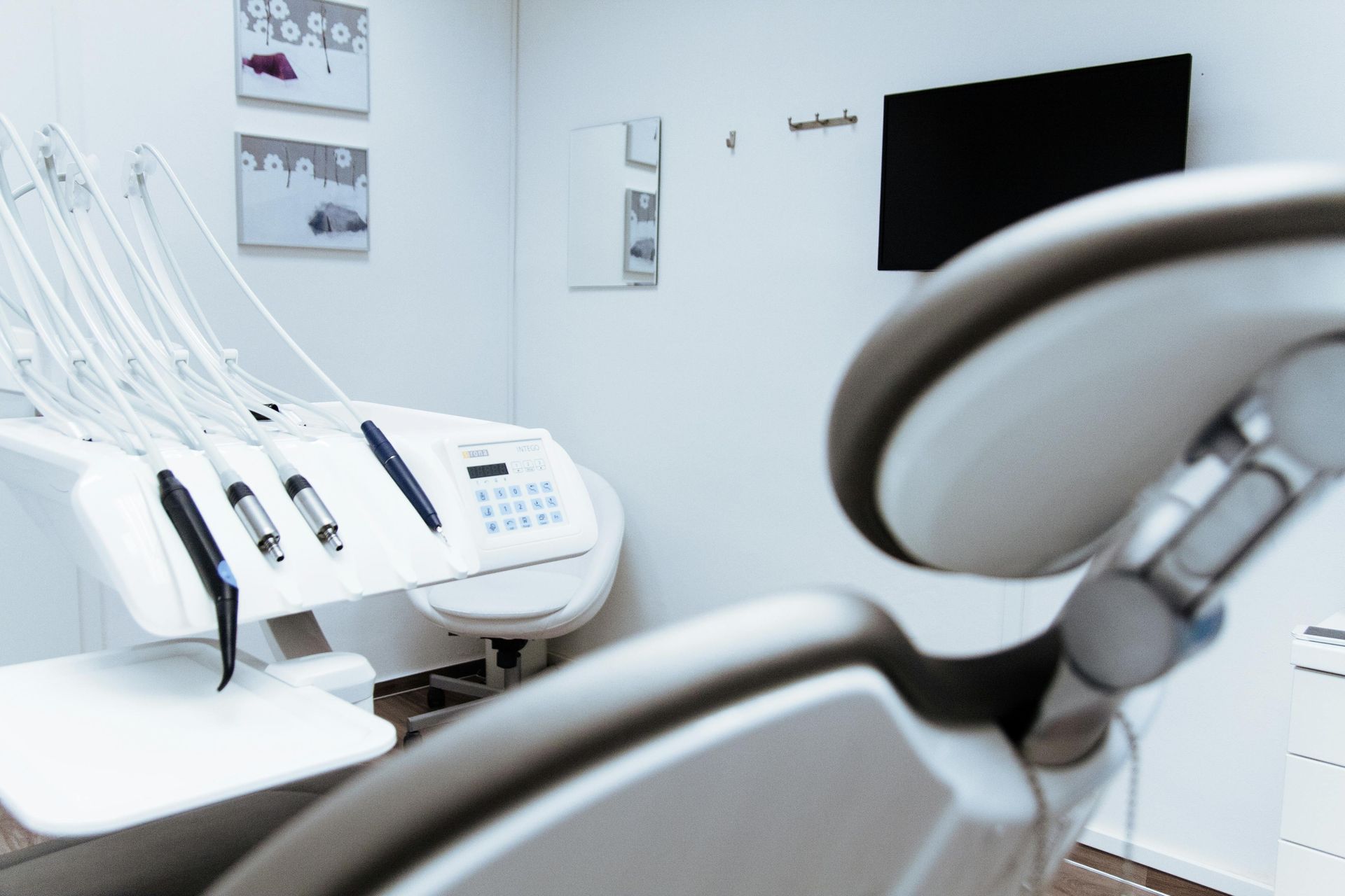 Dentist's office interior: dental chair, equipment, and a mounted monitor. Soft, white color scheme.