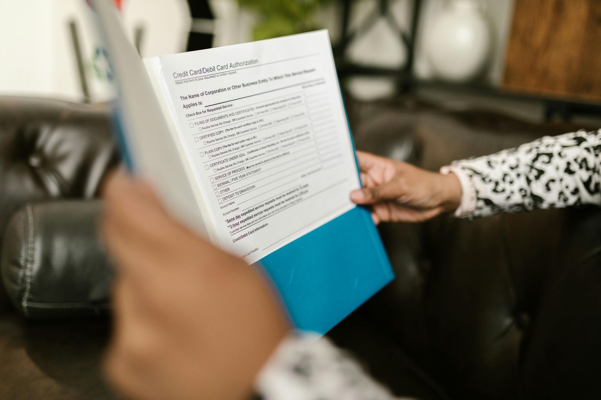 Person holding a blue file folder with a document, sitting on a dark couch.