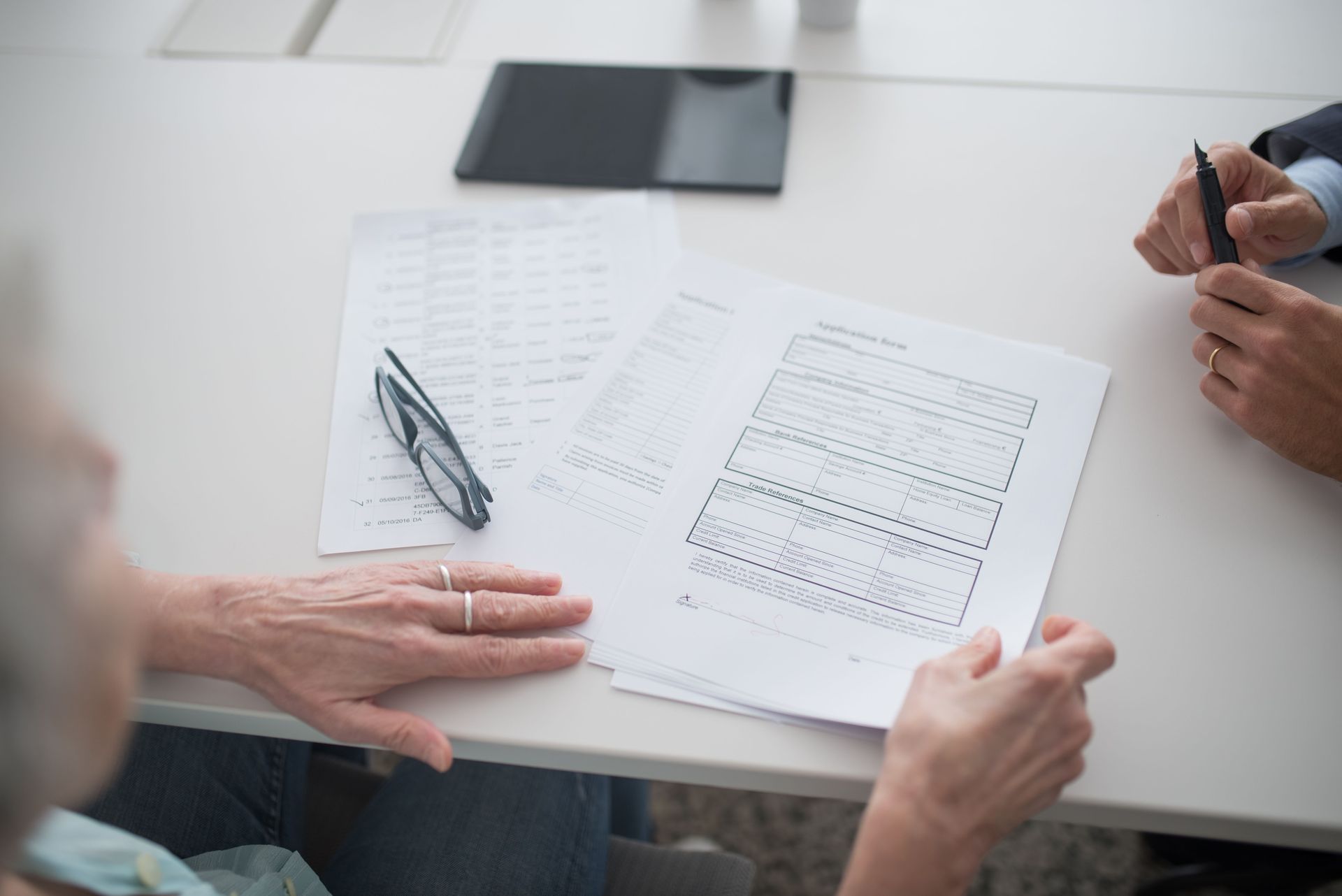 People reviewing printed forms at a white table, with a smartphone and pen nearby.