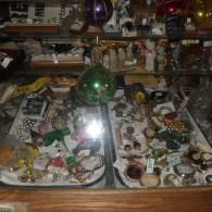 A glass display case filled with various vintage jewelry pieces and trinkets, with large glass spheres hanging above.