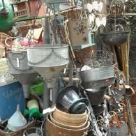 A collection of vintage metal, wooden, and woven gardening items, including hanging funnels and pots in a cluttered shop.