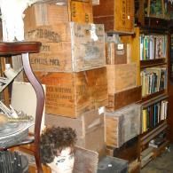 A stacked arrangement of antique wooden crates beside a bookshelf filled with books and a mannequin head.