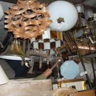 A cluttered collection of various vintage pendant lights, globes, and hanging lamps suspended from a ceiling.
