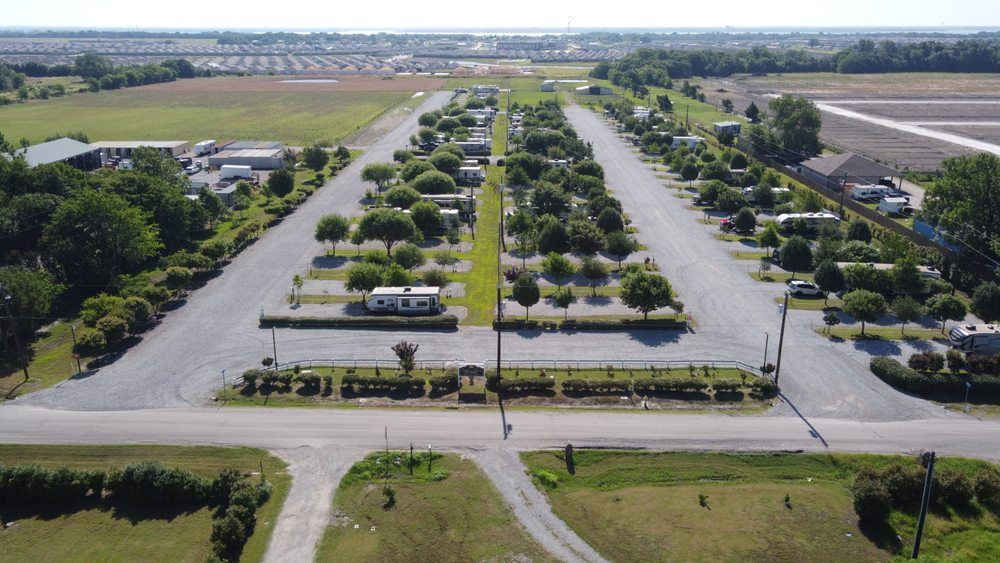 Aerial view of RV park with gravel roads, campsites, trees, and surrounding fields.