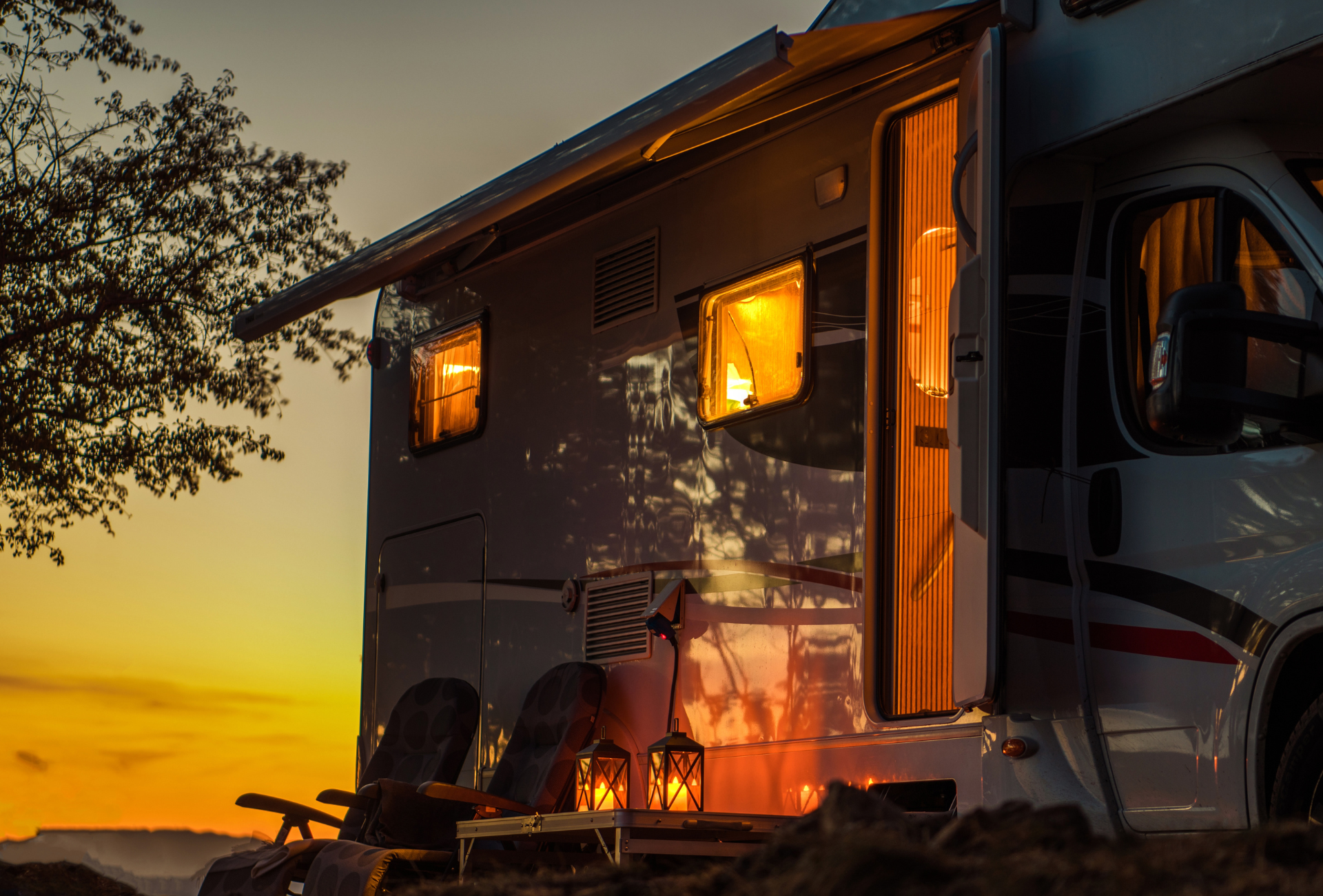 A rv is parked in a field at night with a sunset in the background.