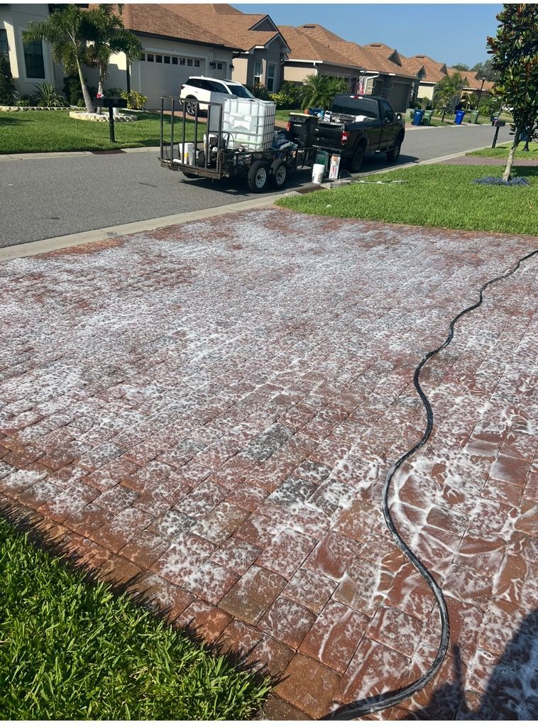 Person using a yellow surface cleaner attached to a pressure washer on a wet concrete surface.
