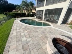 Backyard with a kidney-shaped pool, a paver patio, and a fire pit next to a white house with a screened porch.