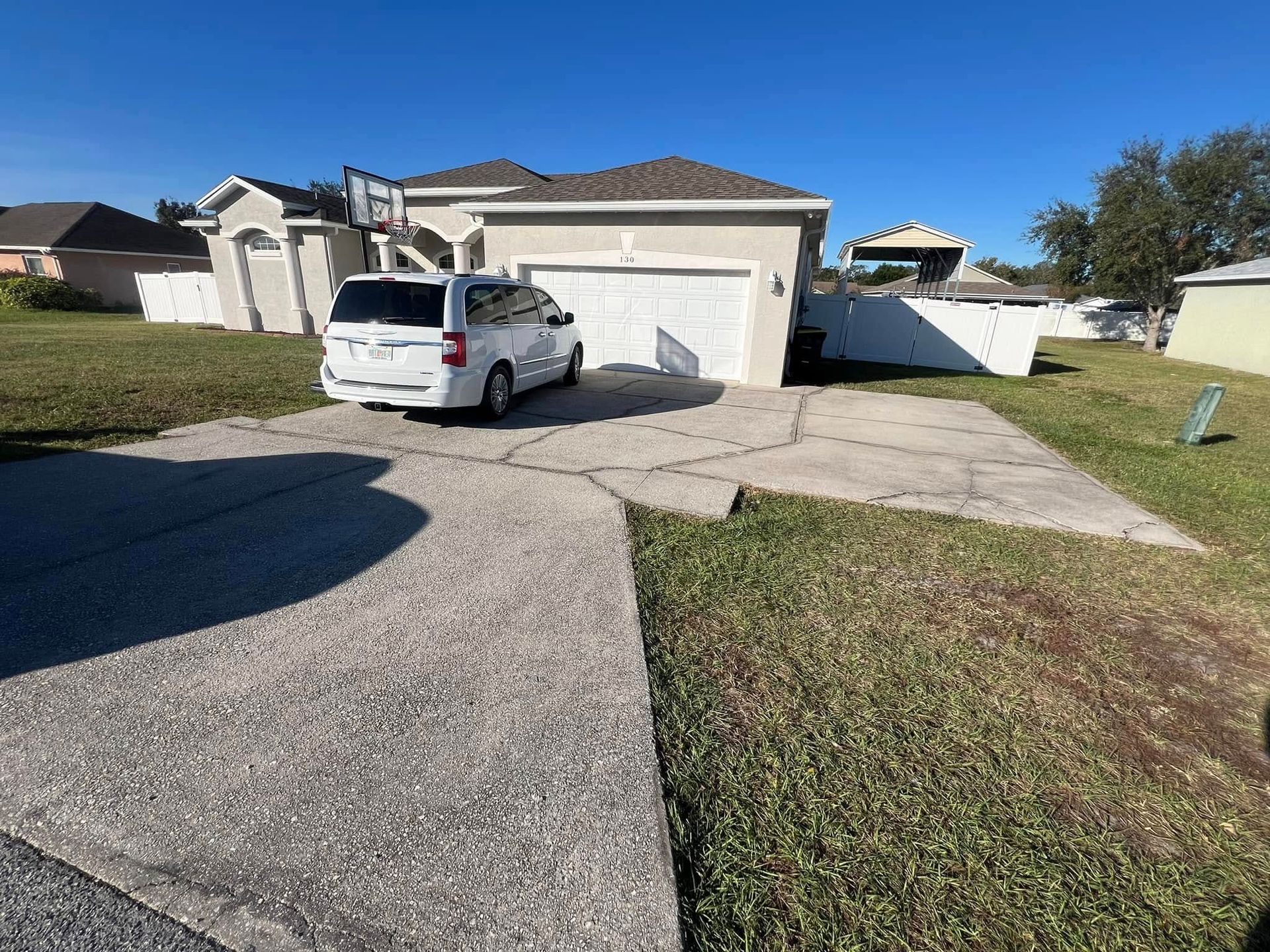A white minivan parked in front of a house with a cracked driveway. The house is beige with a white garage door.