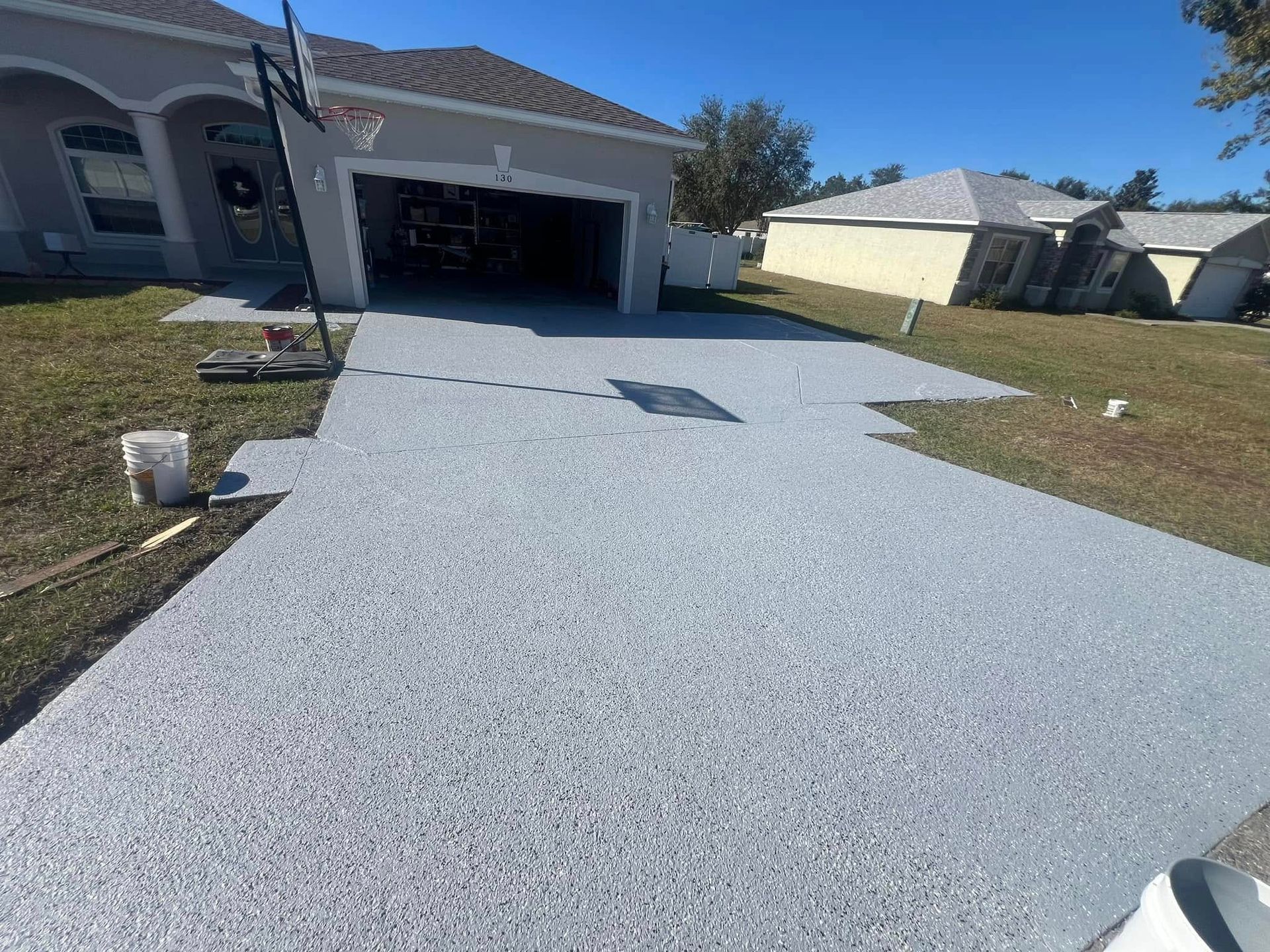 A freshly painted gray epoxy driveway in front of a house on a sunny day.