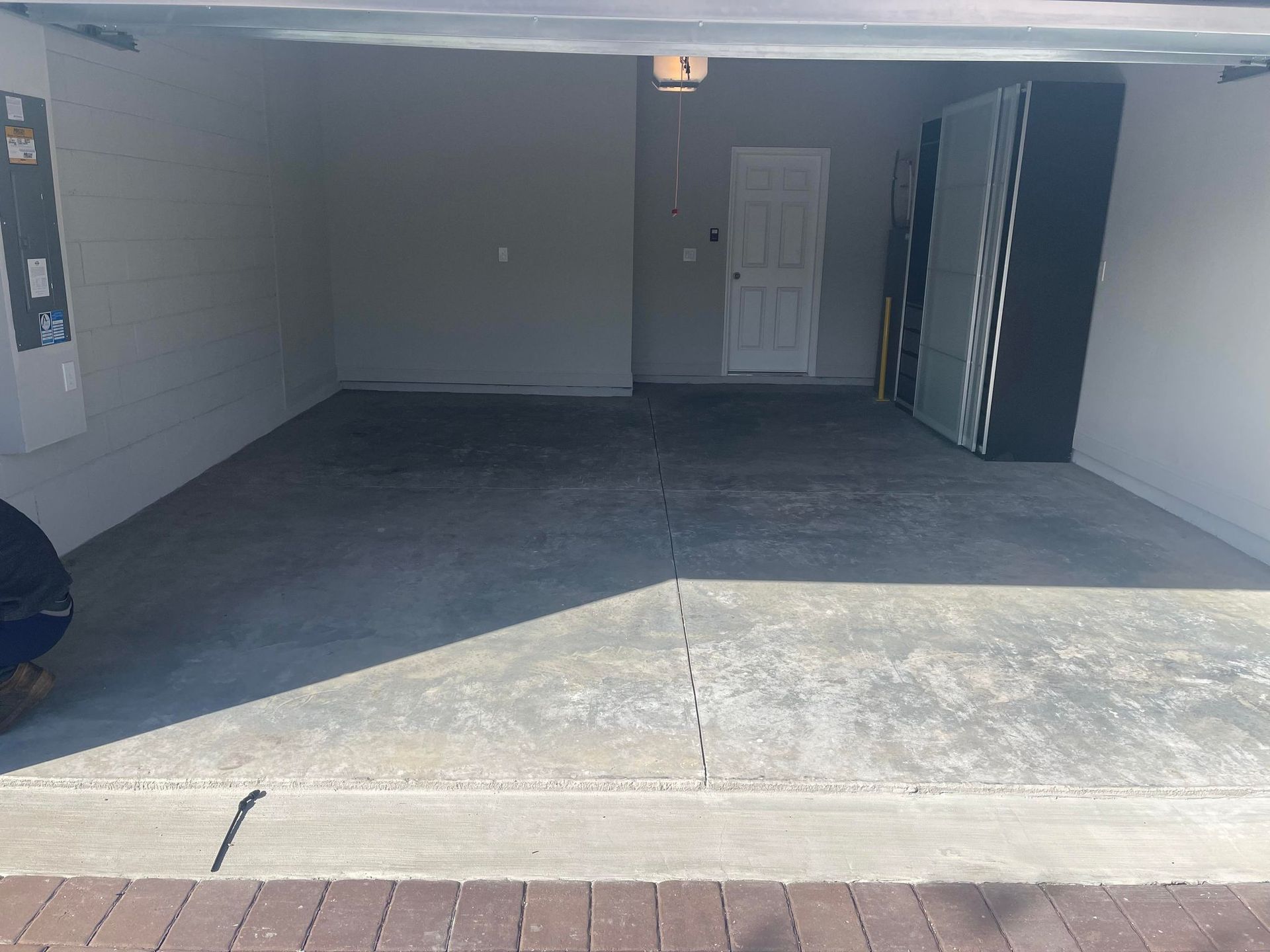 An empty garage with a concrete floor, a white door, and a cabinet against the right wall. The garage door is open.