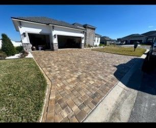 Driveway paved with brown bricks in front of a white house with a garage. Grass borders the driveway.