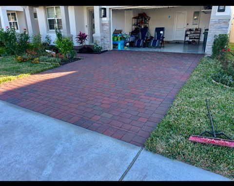 Brick paver driveway leading to a garage, flanked by grass and landscaping.