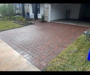 Brick driveway leading to a garage, with a patch of green grass on either side.