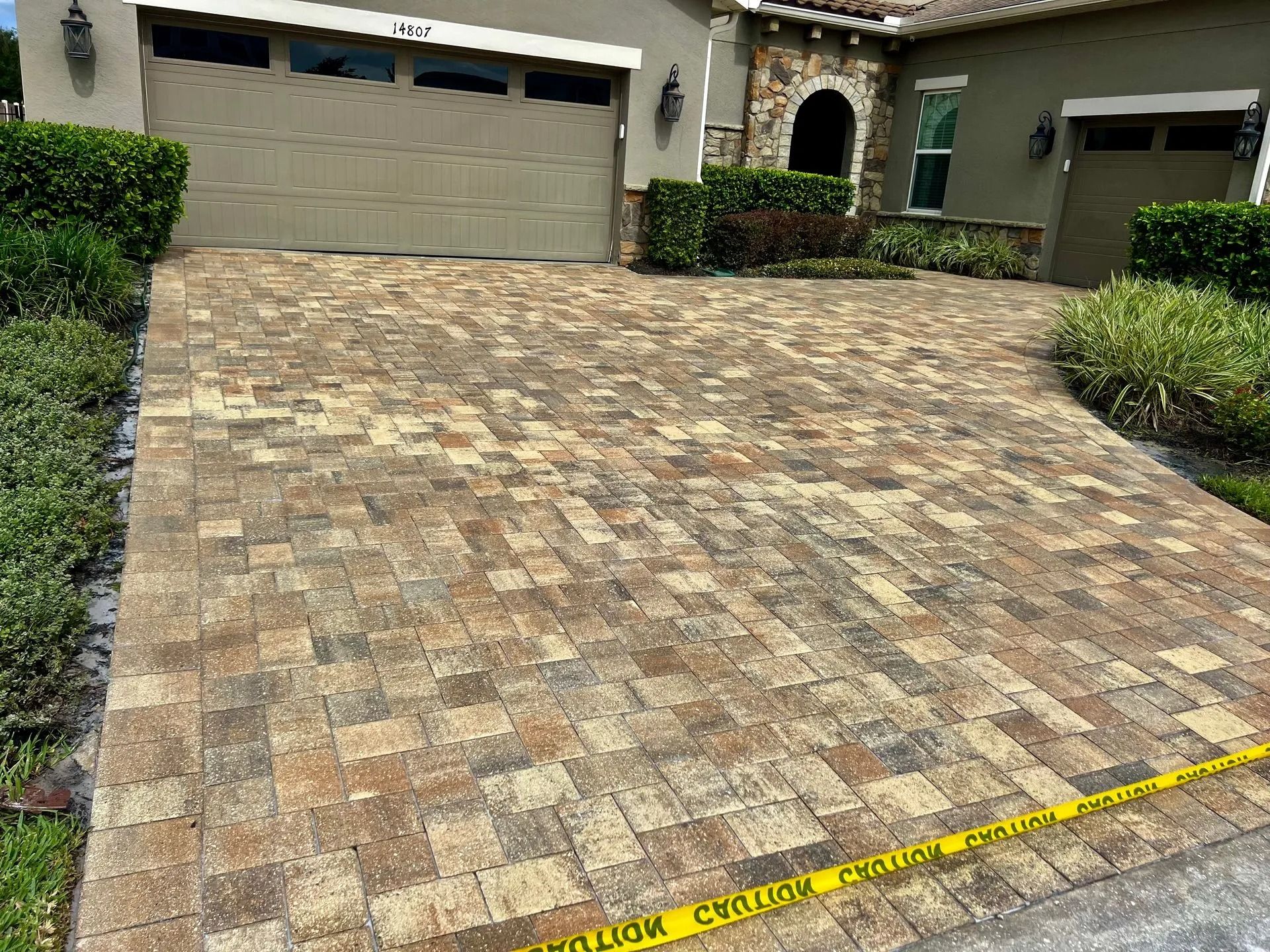 Brick driveway in front of a house with a two-car garage. Yellow caution tape lies on the driveway.