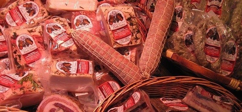 Assortimento di carni confezionate, tra cui salame e pancetta, esposte in un cesto e in altri contenitori.