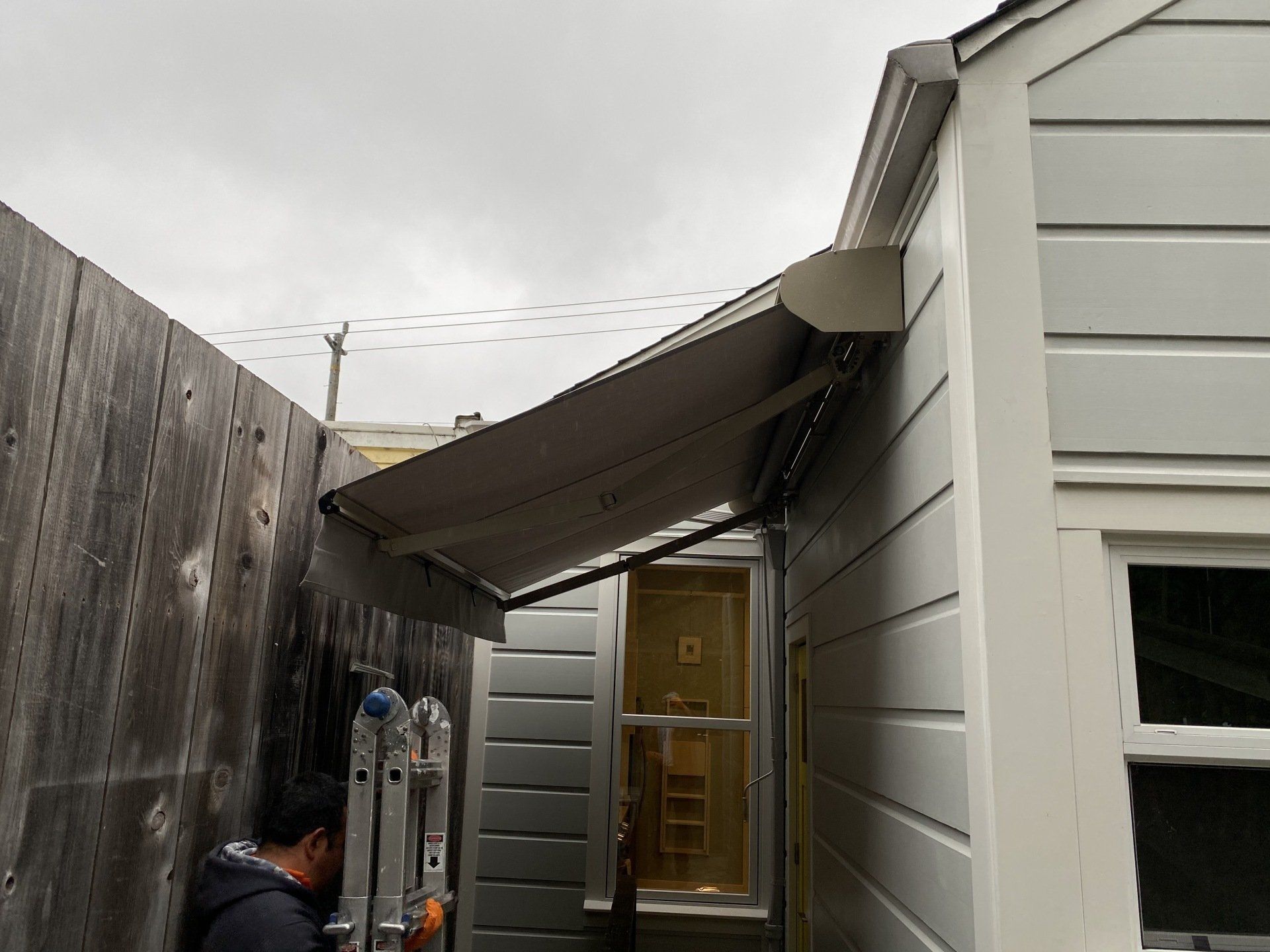 A man is installing an awning on the side of a house.