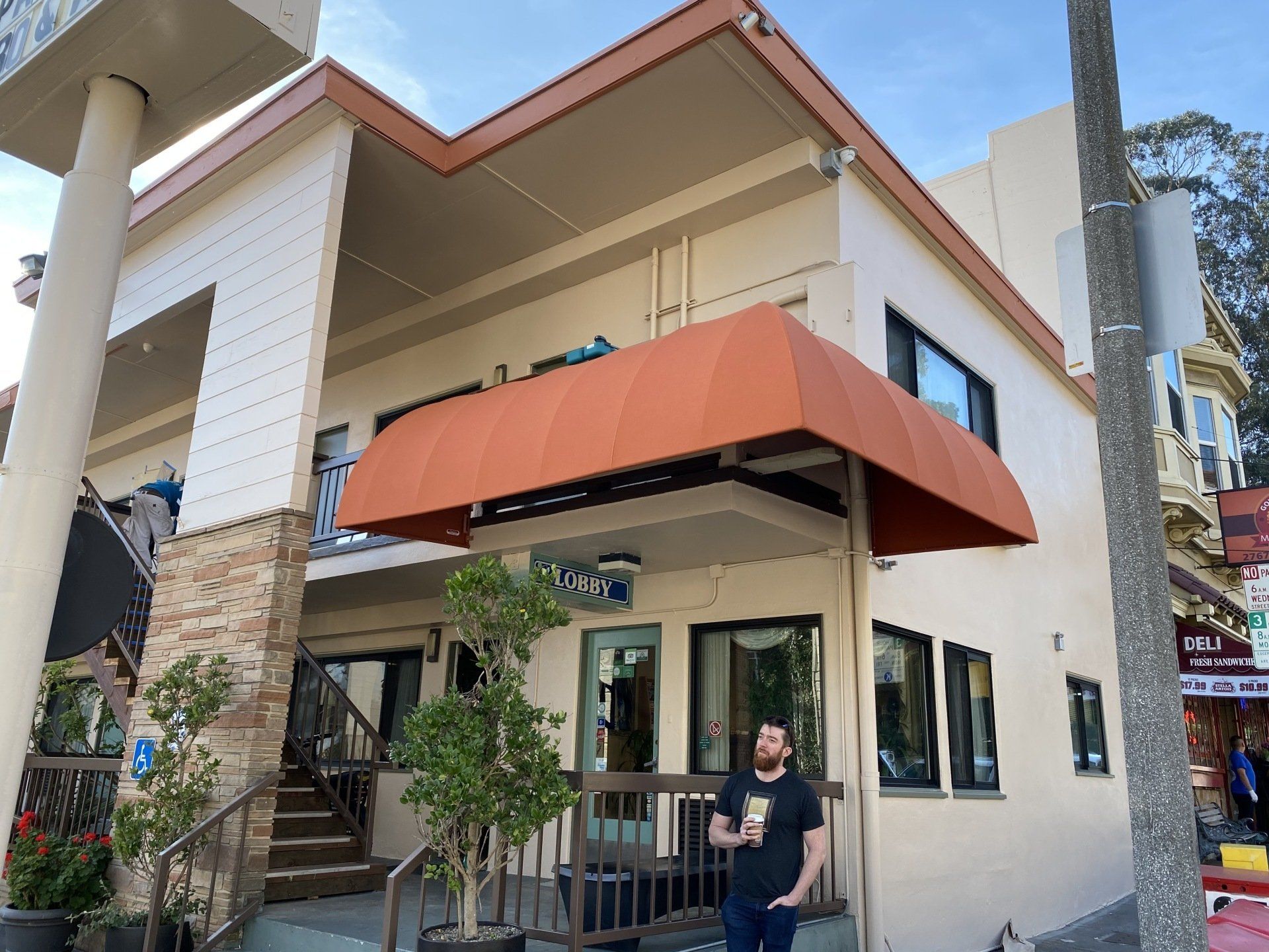 A man stands in front of a building with an orange awning