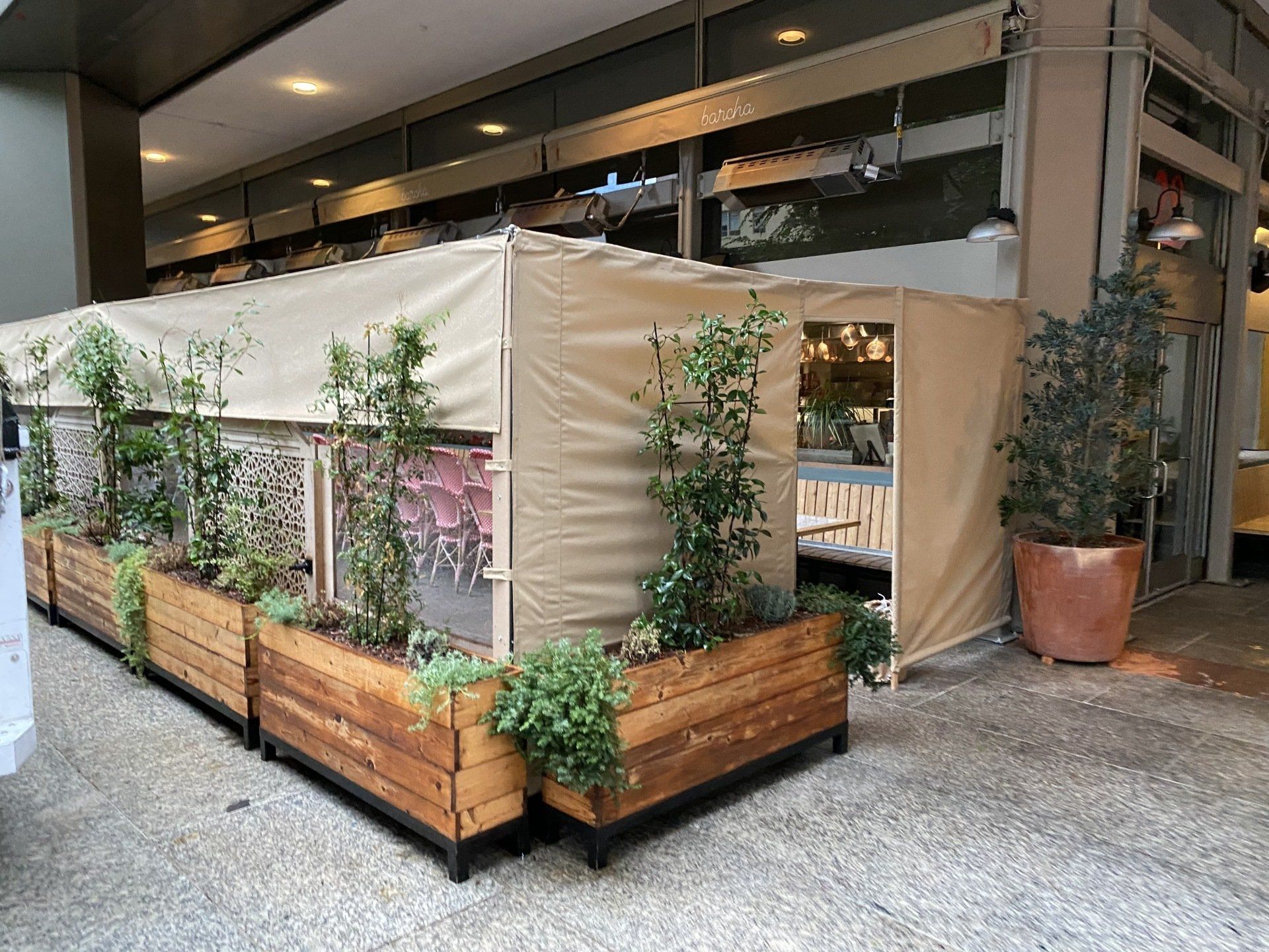 A row of wooden planters with plants and a tent in front of a building.