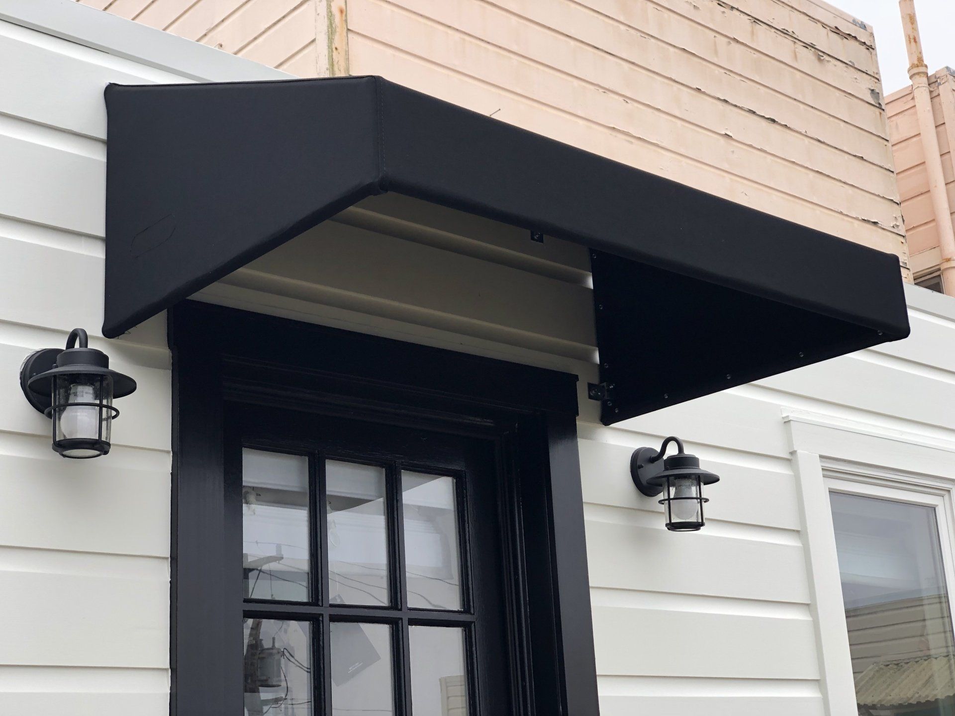 A black awning over a door on a white house.
