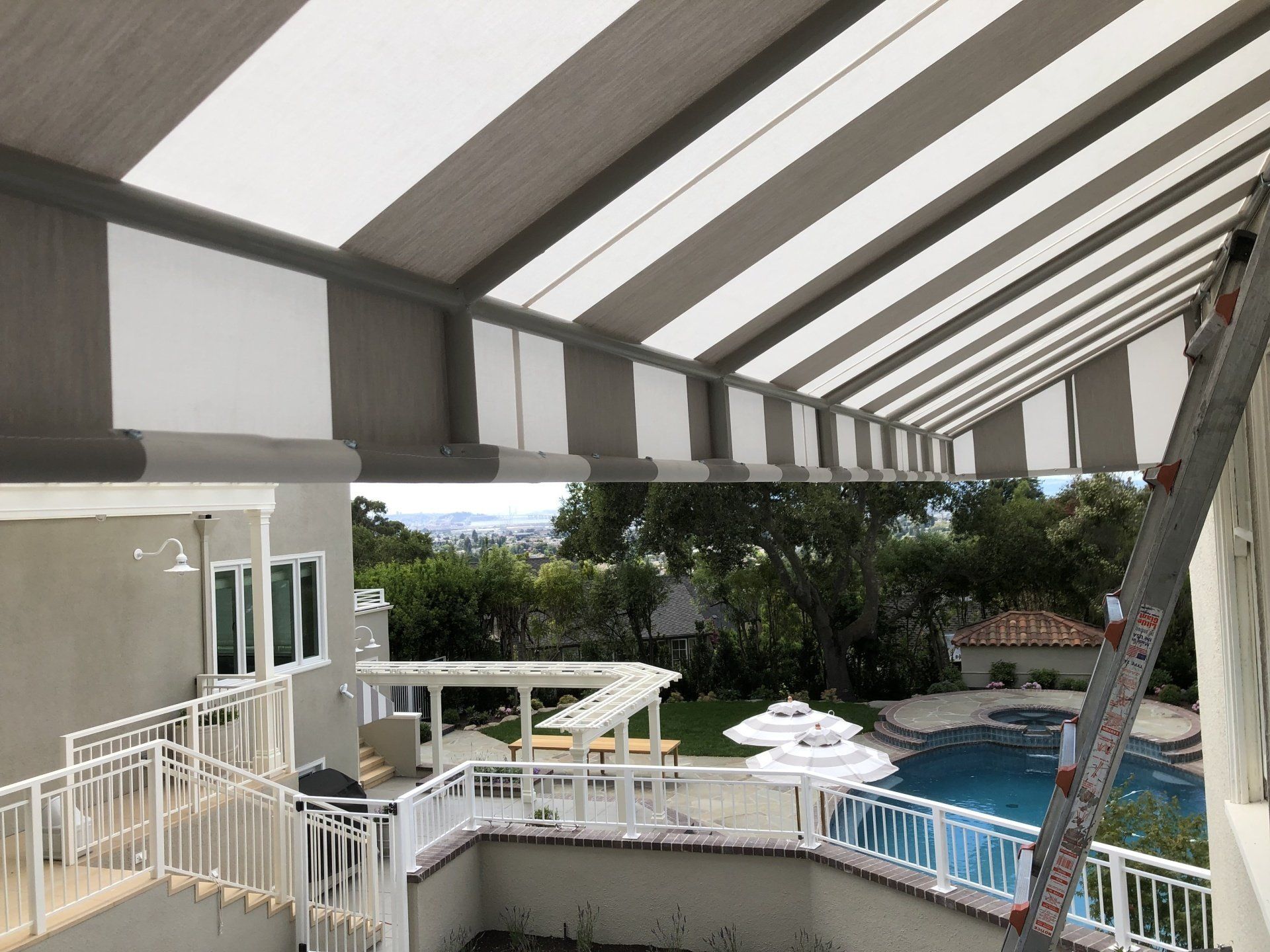 A striped awning is being installed on a patio overlooking a pool.