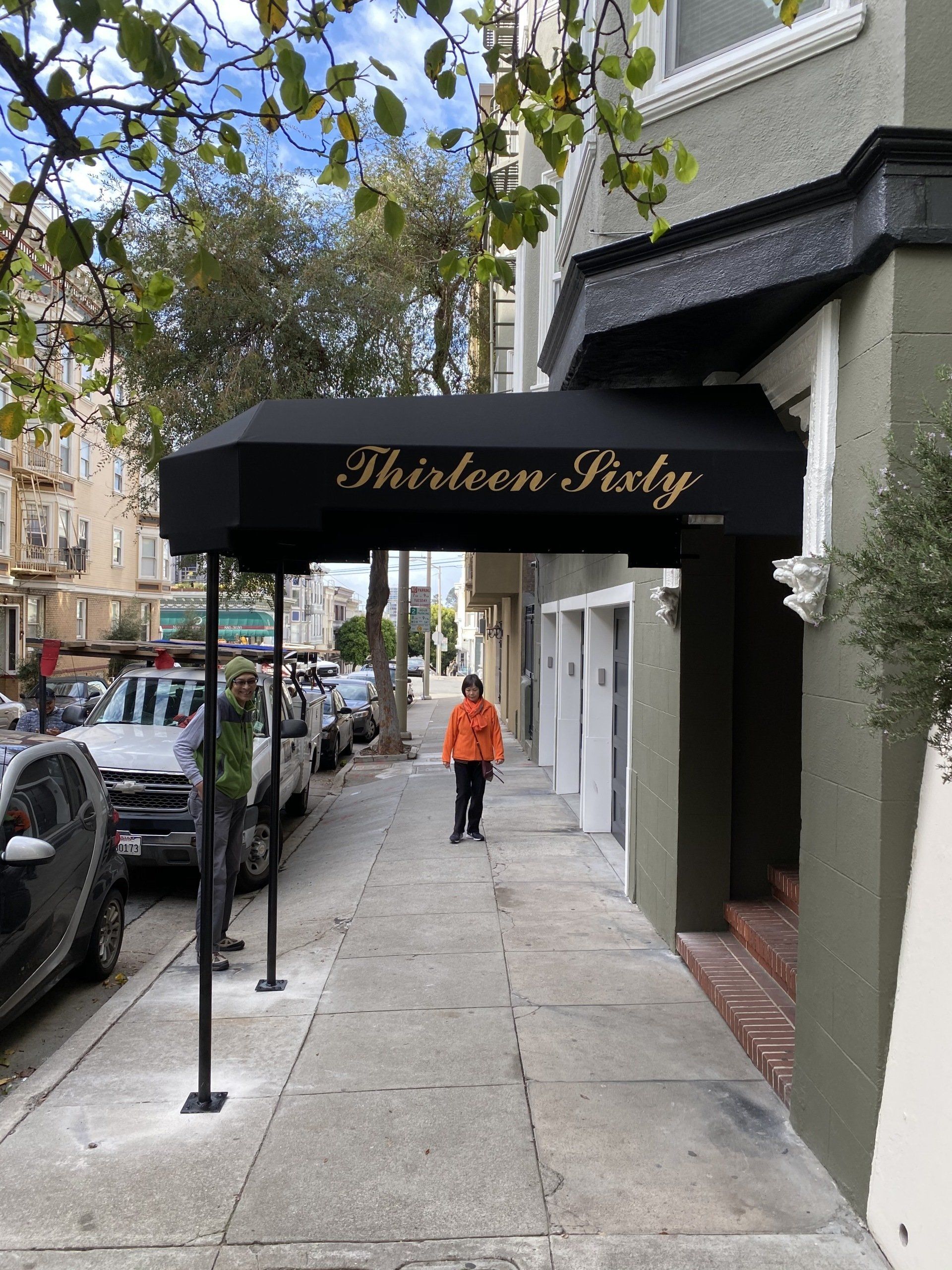A woman is walking down a sidewalk under an awning that says thirteen sixty