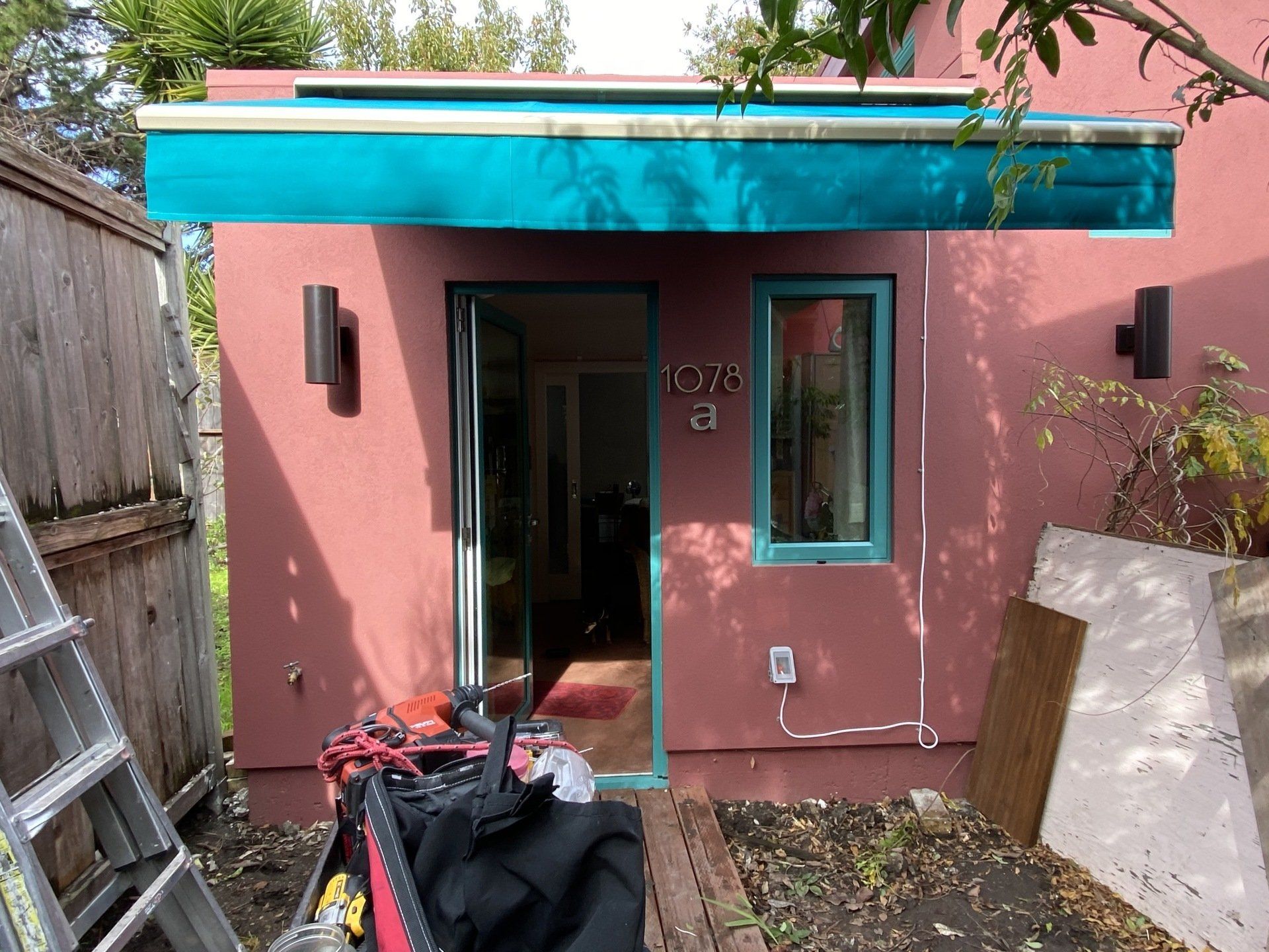 A pink house with a blue awning and a ladder in front of it